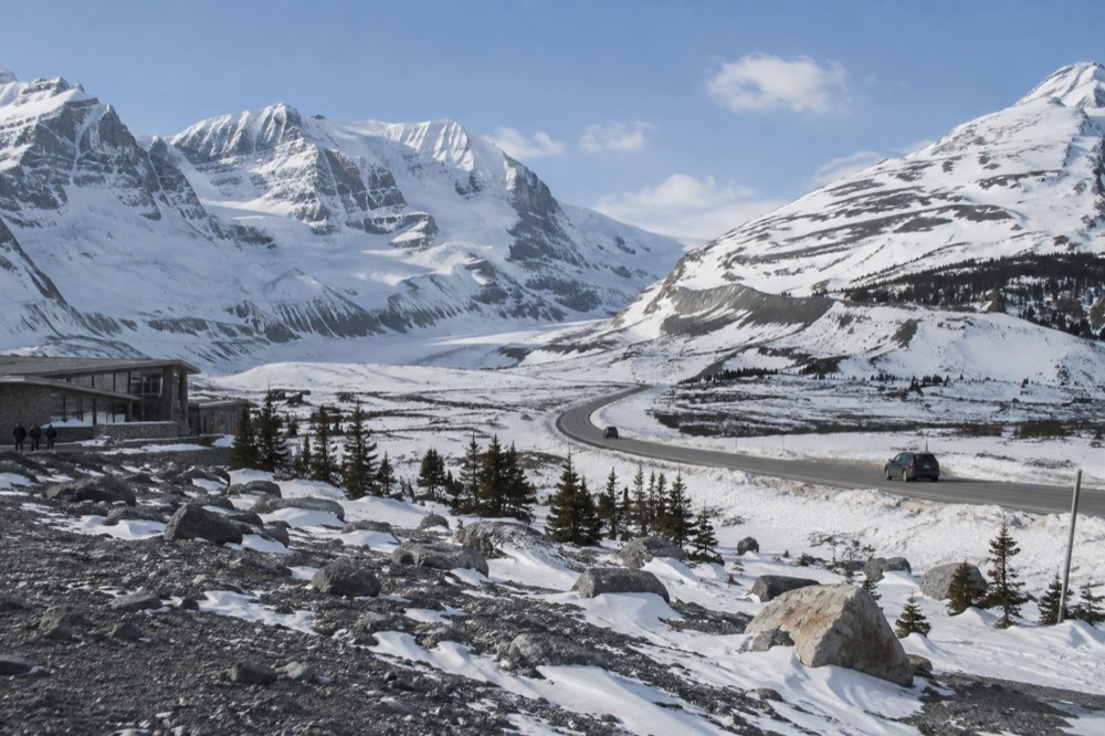A snow-covered highway winding between tall white mountain peaks under clear sky