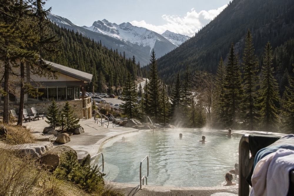 A steaming outdoor hot pool at the base of a forested mountain valley