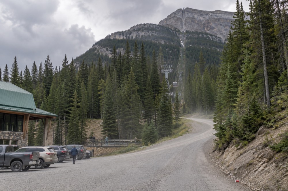 Winding gravel mountain road through forest toward a tall rock face