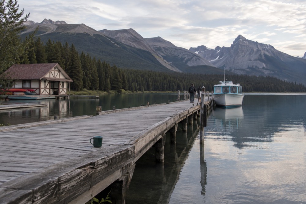 A long wooden dock extending into a calm mountain lake with a tour boat tied up and forested slopes rising behind