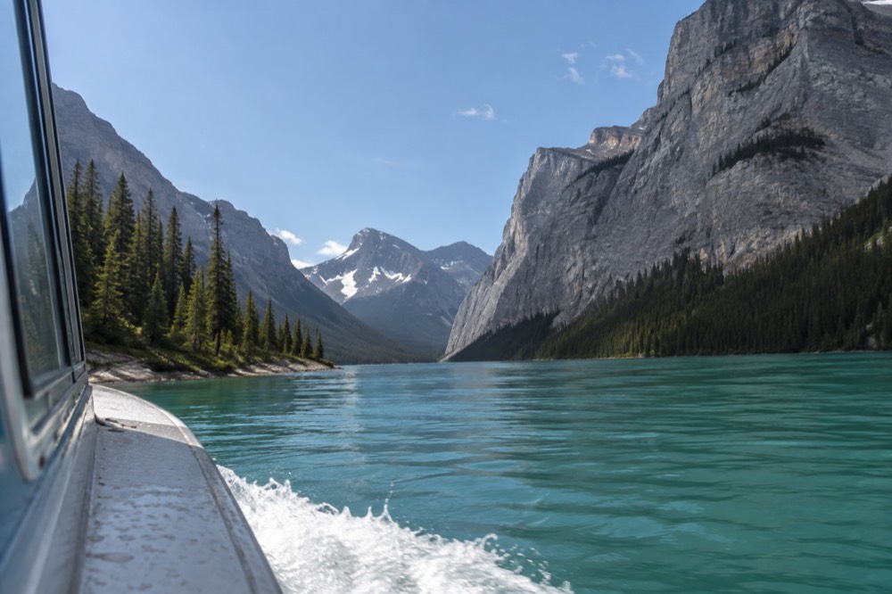 A narrow lake channel with steep rocky walls rising on both sides, the water a deep emerald green under a clear sky