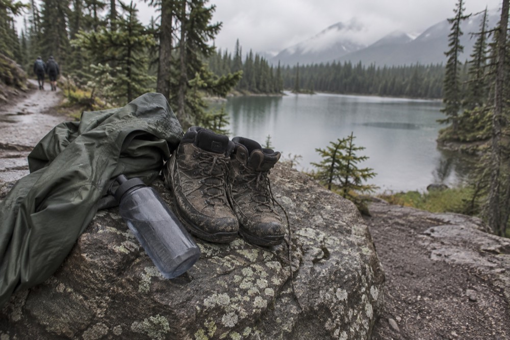 A pair of hiking boots and a rain jacket resting on a rock beside a lake trail