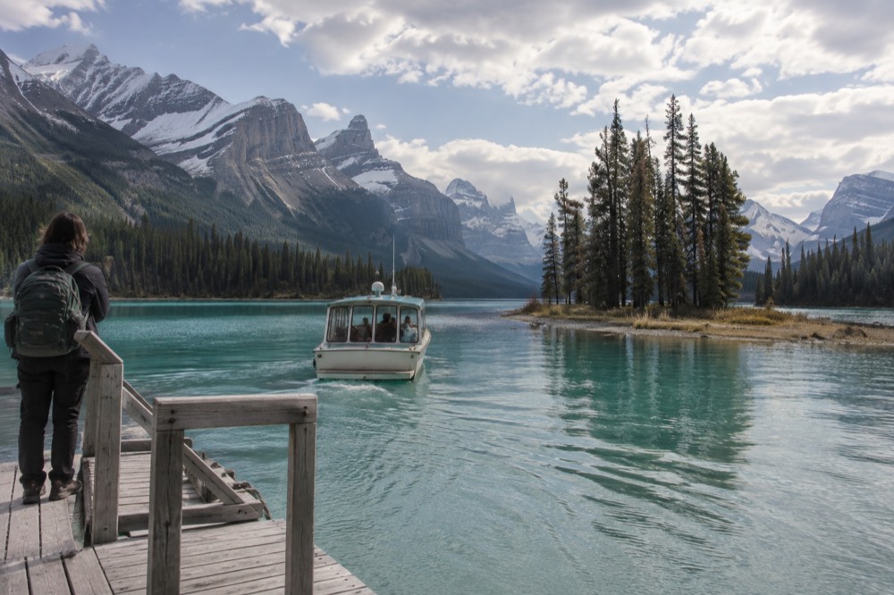 A small boat approaching a tiny tree-covered island in a long mountain lake