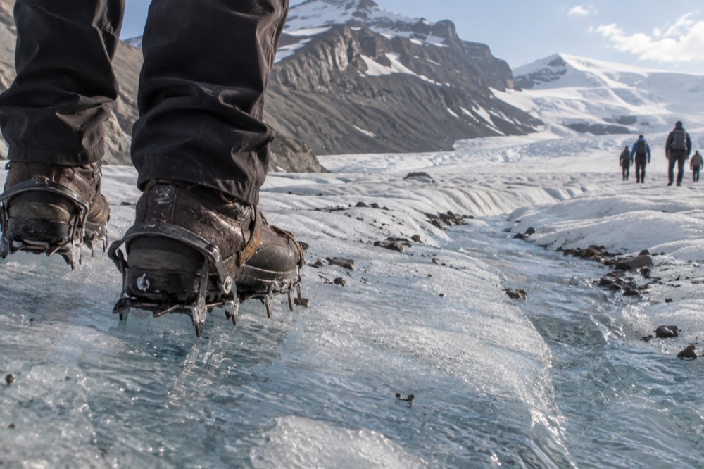Hiking boots and crampons resting on blue glacial ice with meltwater channels nearby