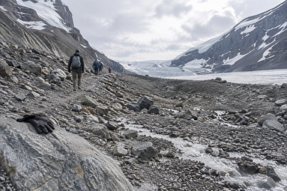 Rocky moraine path leading toward the glacier toe with small meltwater streams crossing the gravel