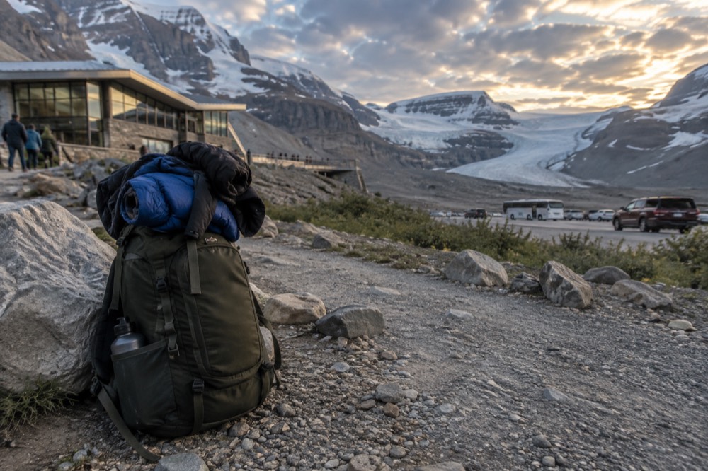 Daypack with layered clothing standing beside a gravel path under a wide mountain sky