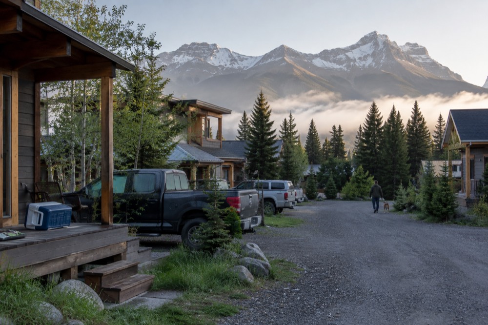 A quiet street in a small mountain town with forested peaks behind the rooftops