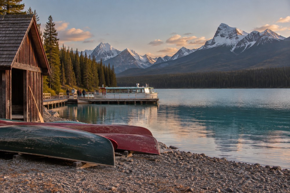 Canoes resting on a shoreline with calm water and mountains in soft evening light